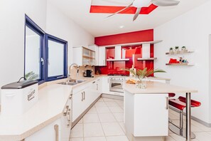 A modern kitchen with white cabinets, a red accent wall, a built-in oven, and a coffee machine. - The ultimate getaway! Spacious layout, luxurious amenities, including a pool. (Oranjestad)