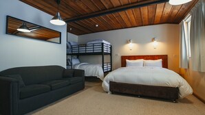 Une pièce comprenant un lit superposé, un canapé et un lit simple. On y trouve deux lampes fixées au mur et un luminaire au plafond.