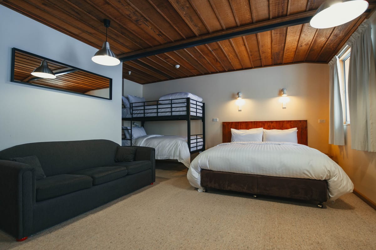 A room with a bunk bed, a sofa, and a single bed. There are two wall-mounted lights and a ceiling light.