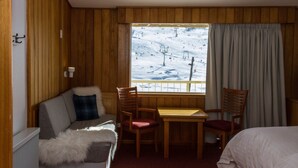 Une chambre d’hôtel avec un décor intérieur en bois, un canapé, une table et une vue sur un paysage enneigé avec un télésiège.