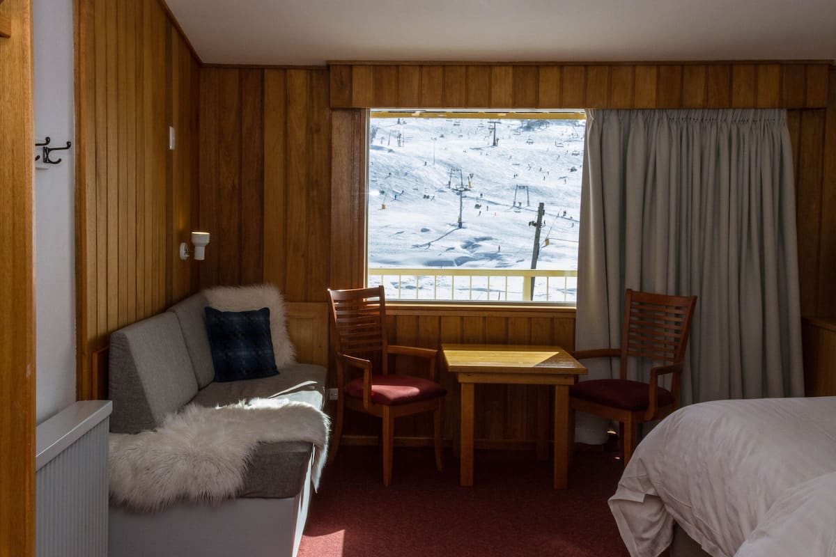 A hotel room with a wooden interior, a sofa, a table, and a view of a snowy landscape with a ski lift.