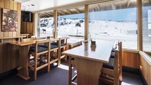 A restaurant with wooden furniture and large windows overlooking a snowy landscape. - Eiger Chalet (Perisher Valley)