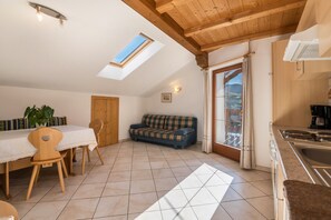 Une pièce comprenant une table à manger, des chaises, un canapé, une lucarne, un coin cuisine et une vue par la fenêtre.