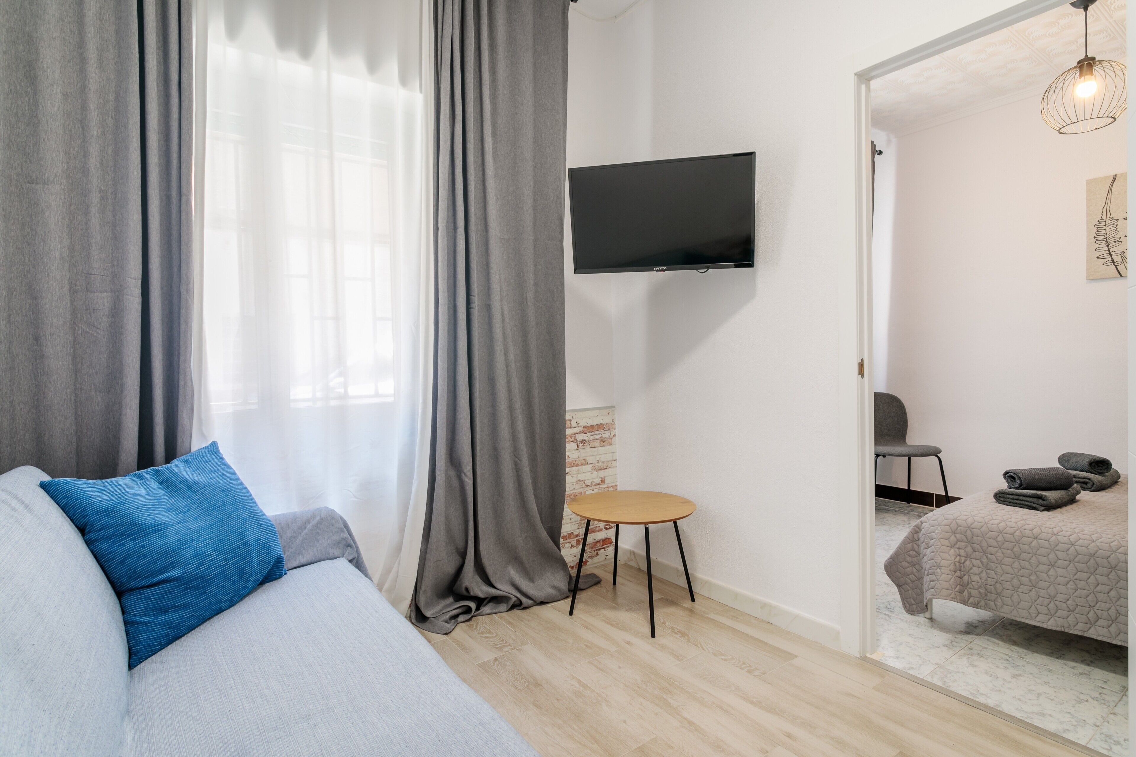 Une chambre moderne avec un canapé, une petite table ronde, un téléviseur fixé au mur et un lit avec une tête de lit.
