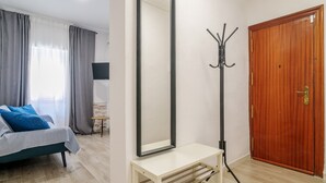 Une pièce avec un lit, un porte-manteau, une porte en bois et un mur blanc.