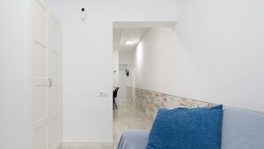 Un couloir avec une armoire blanche, un canapé gris agrémenté d’un coussin bleu et un mur au motif de briques.
