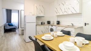 Une cuisine moderne avec un coin repas, un pare-feu en marbre blanc et un lit recouvert d’une couverture bleue.