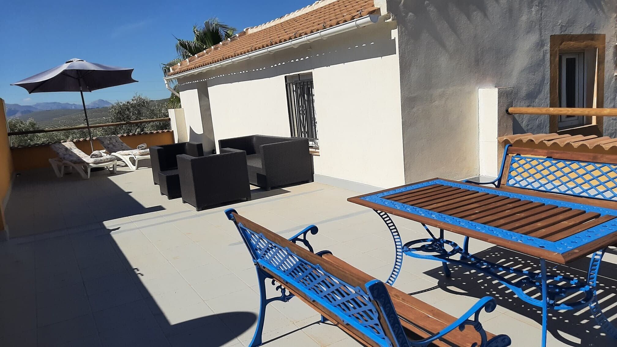 A terrace with a table and benches, a view of the mountains, and a building with a tiled roof.