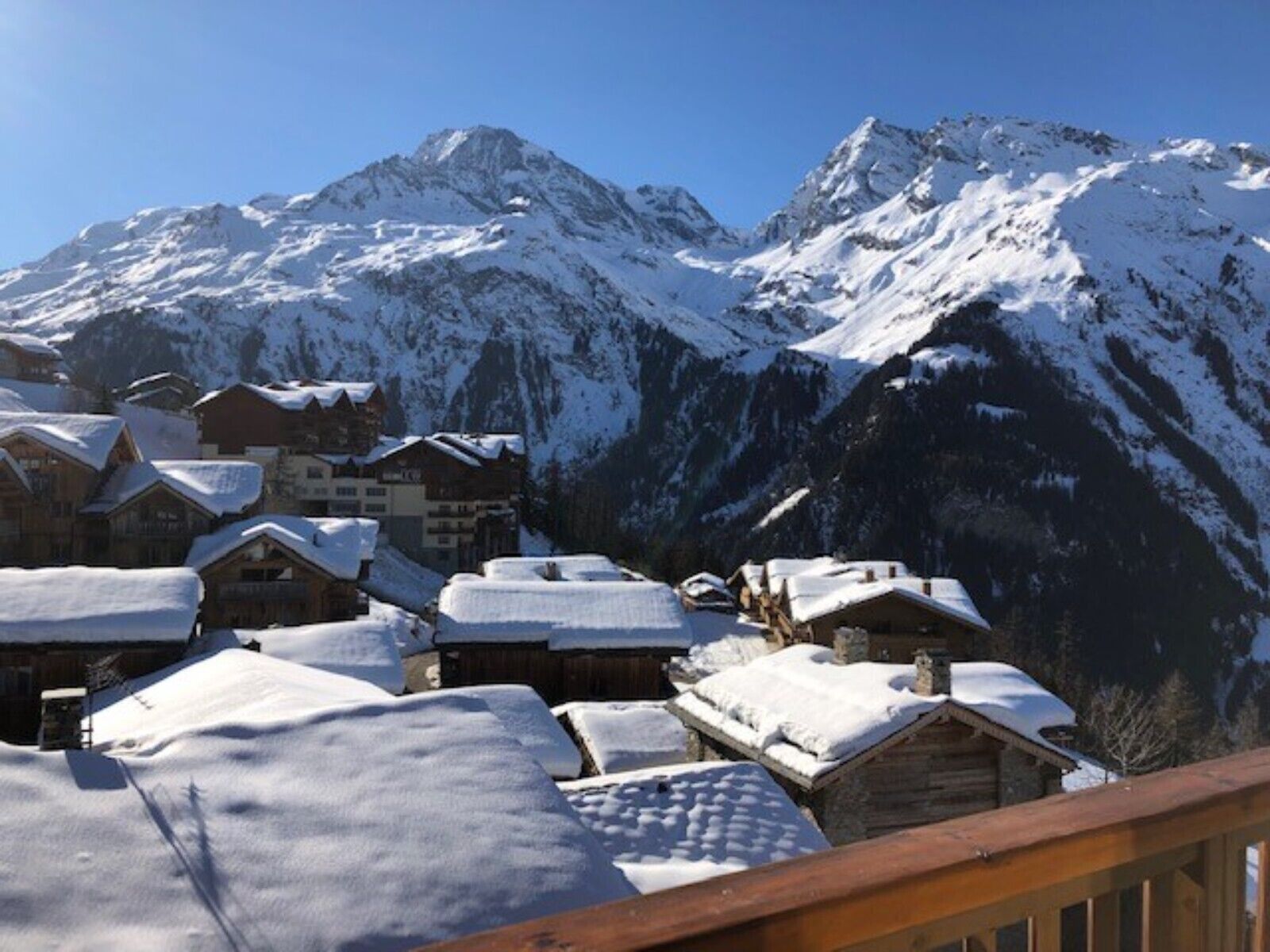 A snow-covered mountain village with wooden buildings and a clear view of the surrounding peaks.