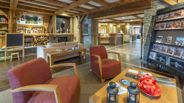 Eine geräumige Lobby mit Holzbalken, einer Steinwand, einem Empfangsbereich und einer Sitzecke mit roten Stühlen und einem Couchtisch.