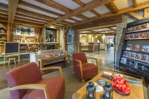 A spacious lobby with wooden beams, a stone wall, a reception desk, and a seating area with red chairs and a coffee table.