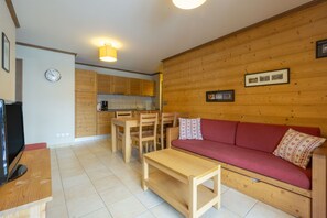 Ambiente in legno con divano, televisore, tavolo di legno e angolo cottura.