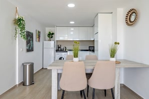 A modern kitchen with white cabinets, a stainless steel trash can, and a dining area with a wooden table and two chairs. - Apartment 'Francesca' with Shared Pool, Wi-Fi and Air Conditioning (Vinaros)