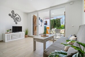 Een woonkamer met een bank, een televisie op een kast, een tafel en een schuifpui naar een buitenruimte.
