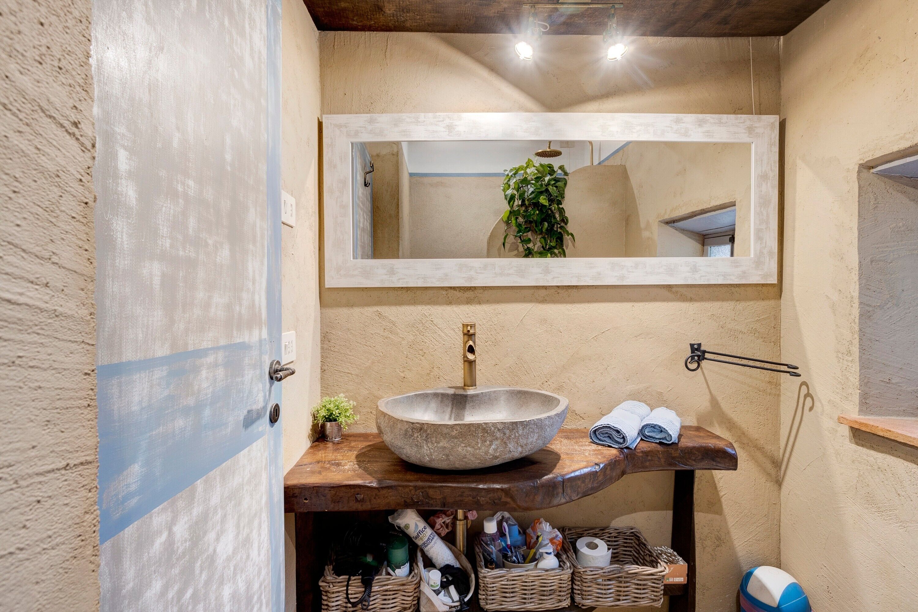 A bathroom with a large stone sink, a mirror above it, and a shelf with towels and toiletries.