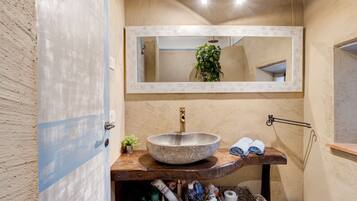 A bathroom with a large stone sink, a mirror above it, and a shelf with towels and toiletries.