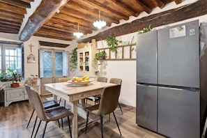 A kitchen with a wooden table, chairs, a refrigerator, and hanging plants.