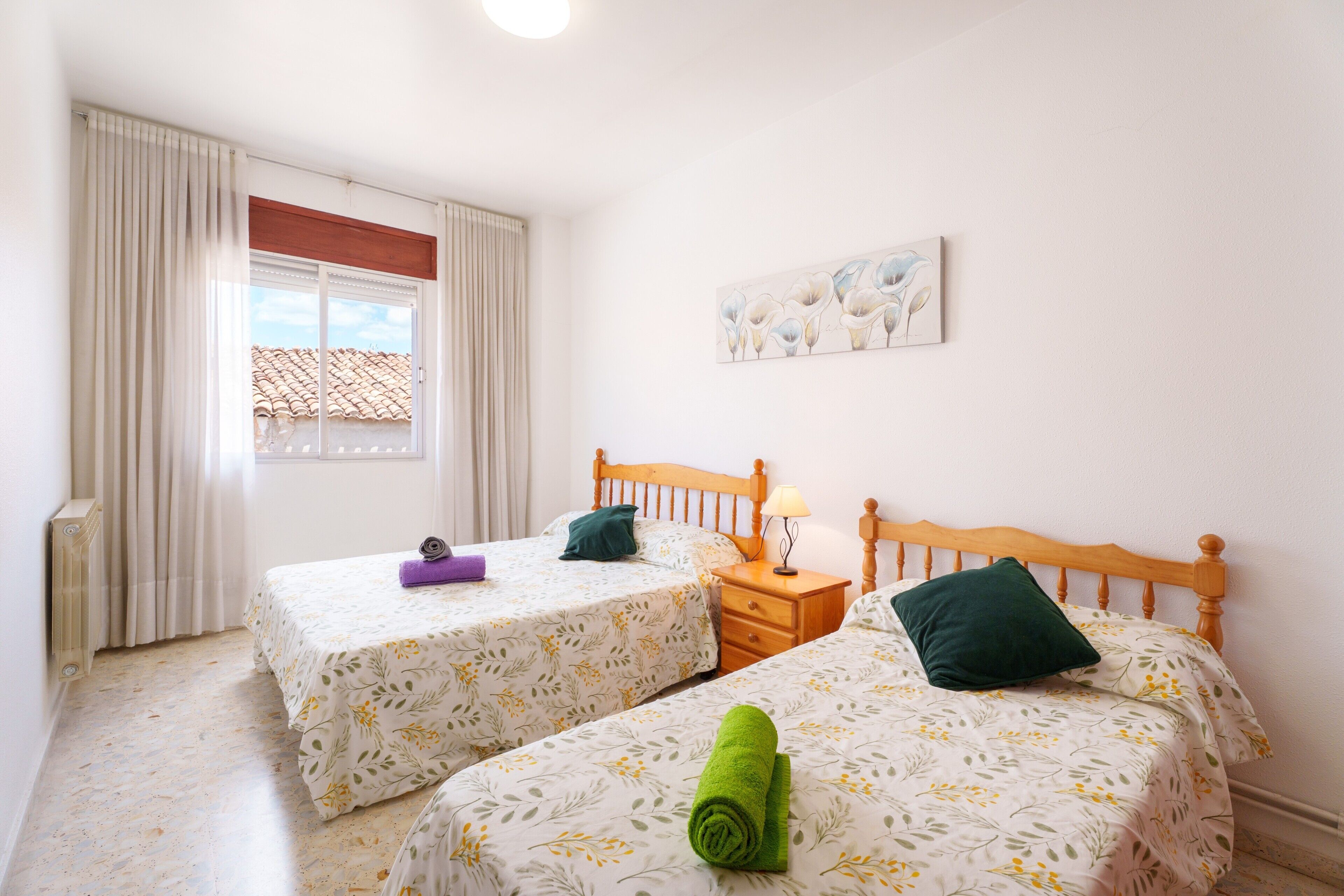 Habitació d'hotel amb dos llits, una finestra amb cortines, una tauleta de nit i un quadre penjat a la paret.