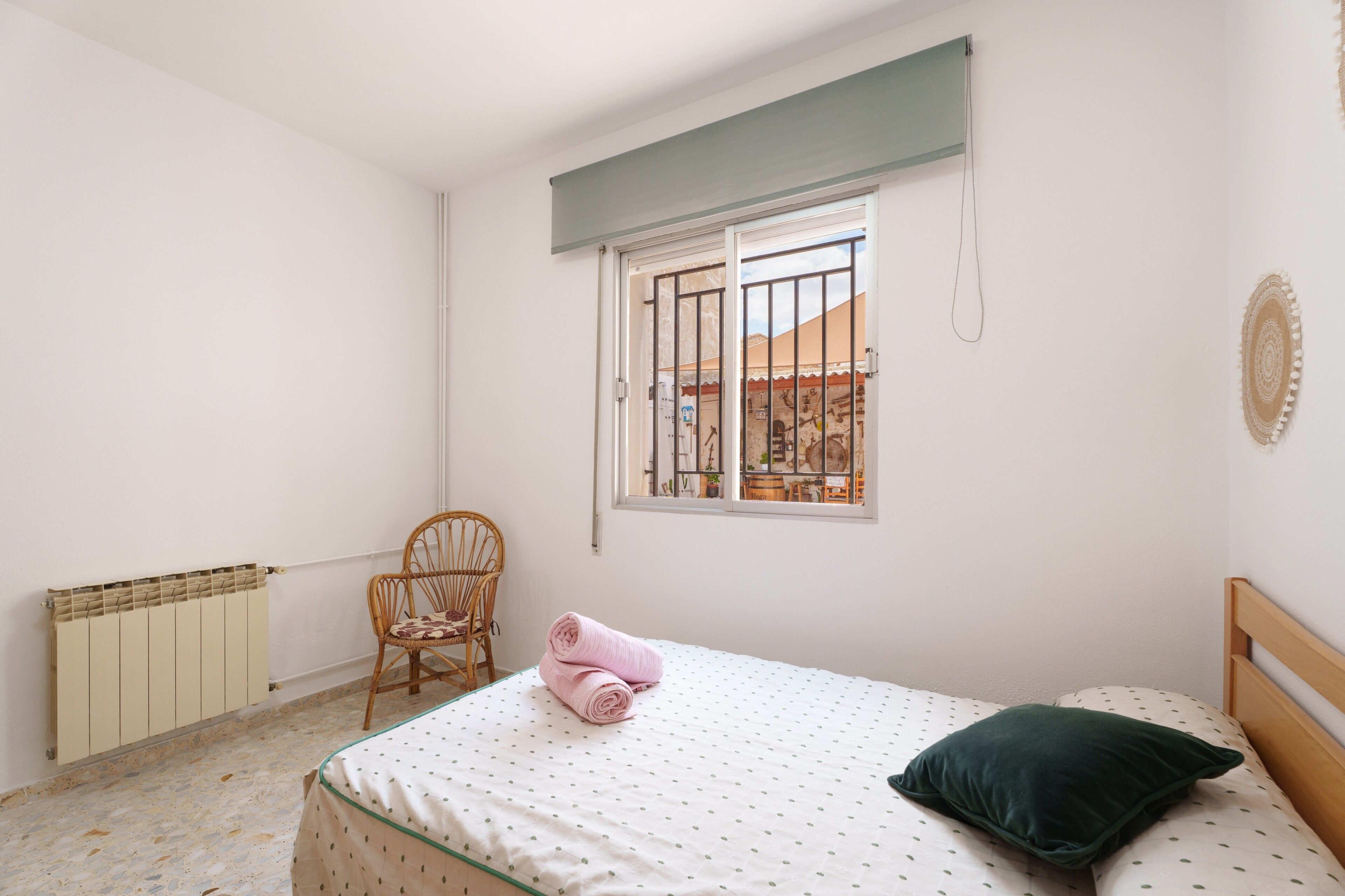 Un dormitorio con cama, una silla, un radiador, un ventanal y vistas al exterior.