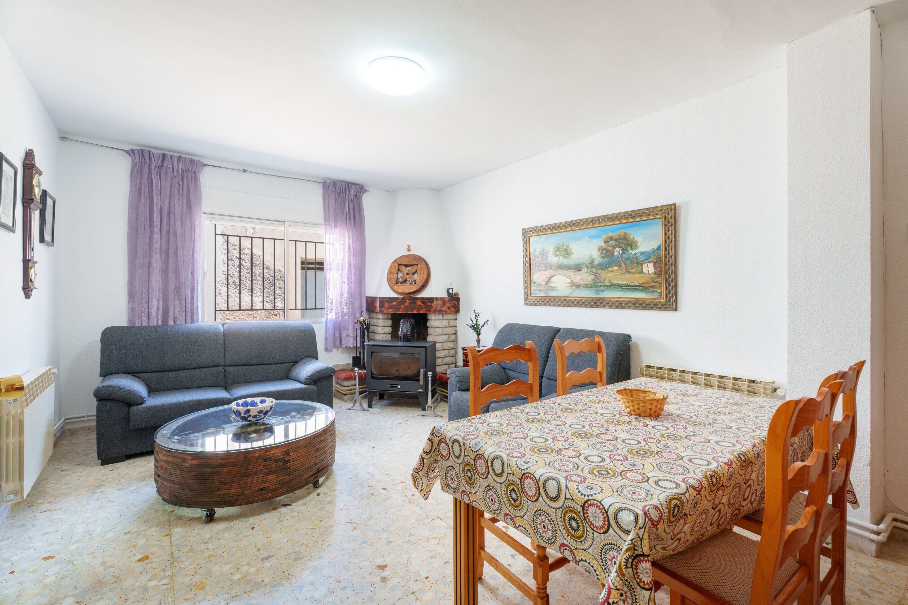 A living room with a sofa, a coffee table, a dining table with chairs, a fireplace, and a painting on the wall.