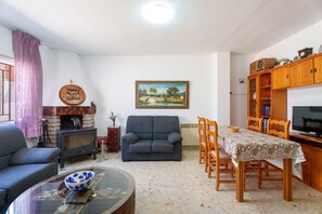 A living room with a sofa, a TV, a fireplace, a dining table with chairs, and a bookshelf.