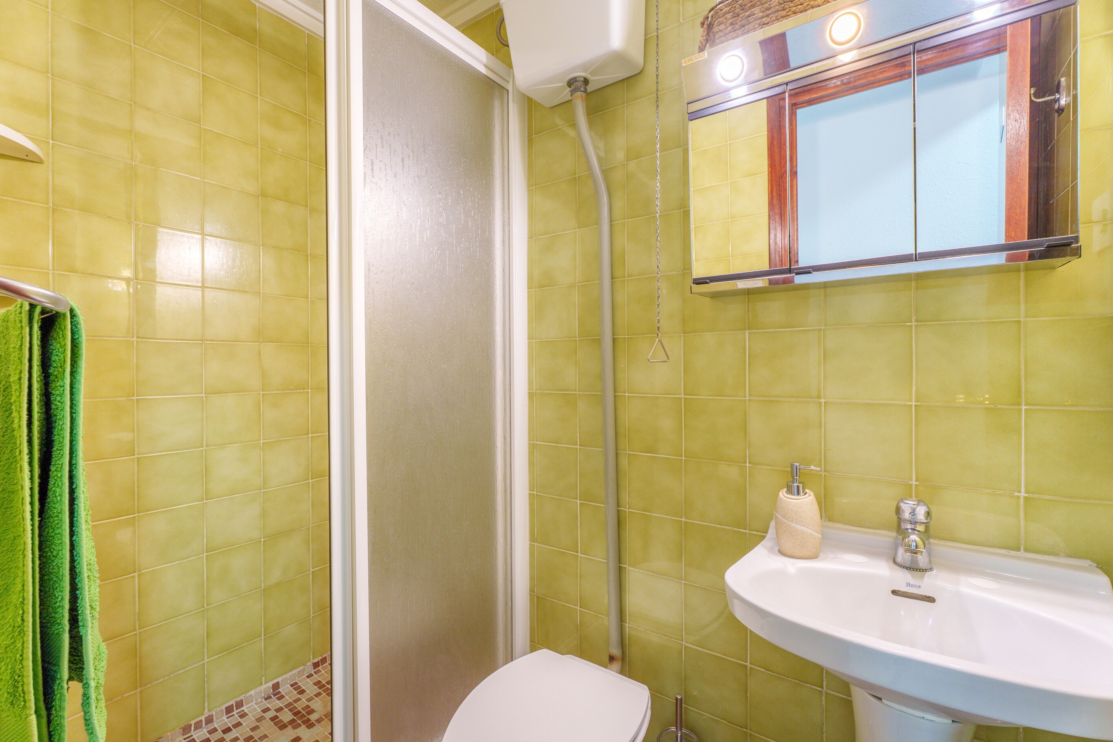A bathroom with yellow tiles, a white sink, a mirror with a wooden frame, and a green towel.