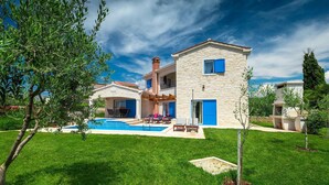 Une maison en pierre à deux étages, dotée d’une piscine, d’un espace extérieur aménagé et d’une pelouse bien entretenue.