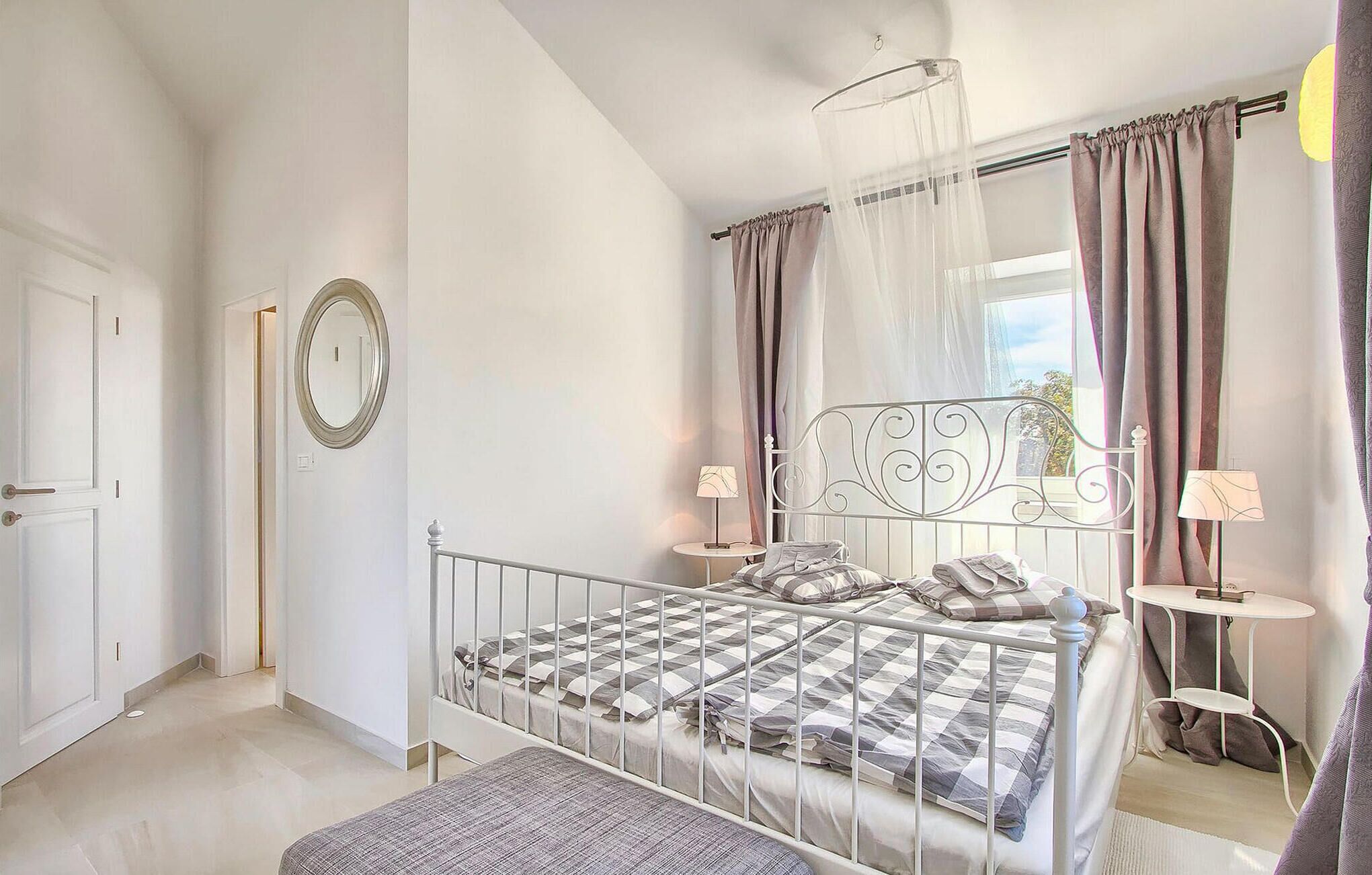 A bedroom with a bed, bedside tables, a mirror, and curtains.