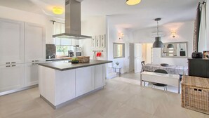 Une cuisine moderne avec des meubles blancs, un îlot central et un coin repas doté d’une table en marbre.