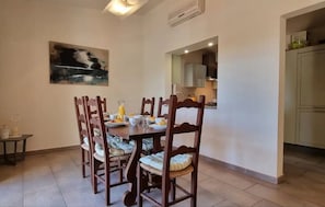 A dining area with a table set for four, wooden chairs with cushioned seats, a painting on the wall, and a kitchen visible through an archway. - Villa 'Casa Florencia' with Wi-Fi and Air Conditioning (Loulé)