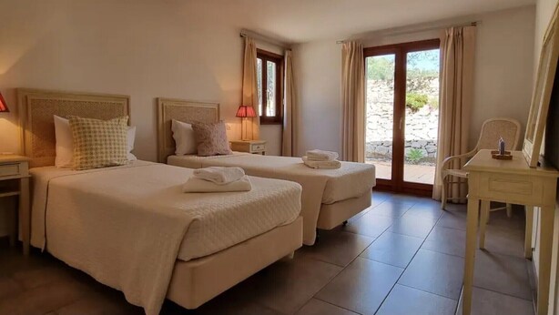 A hotel room with two beds, a desk, and a view of the outdoors.