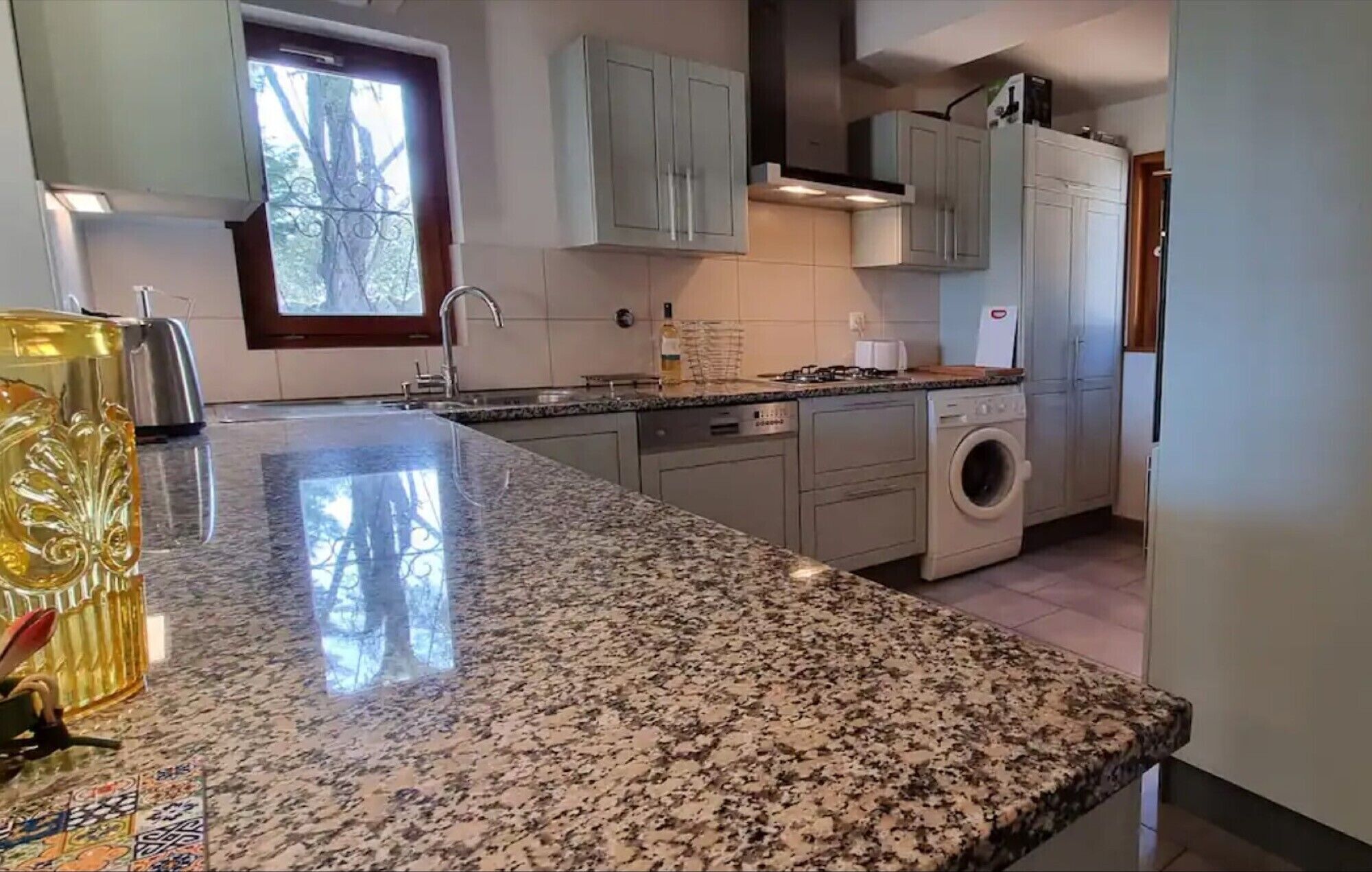 A kitchen with granite countertops, a built-in washing machine, and light-colored cabinets.