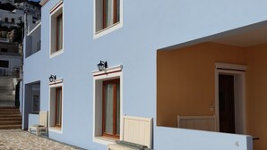 A two-story building with a light blue facade, a stone-tiled courtyard, and a bench.