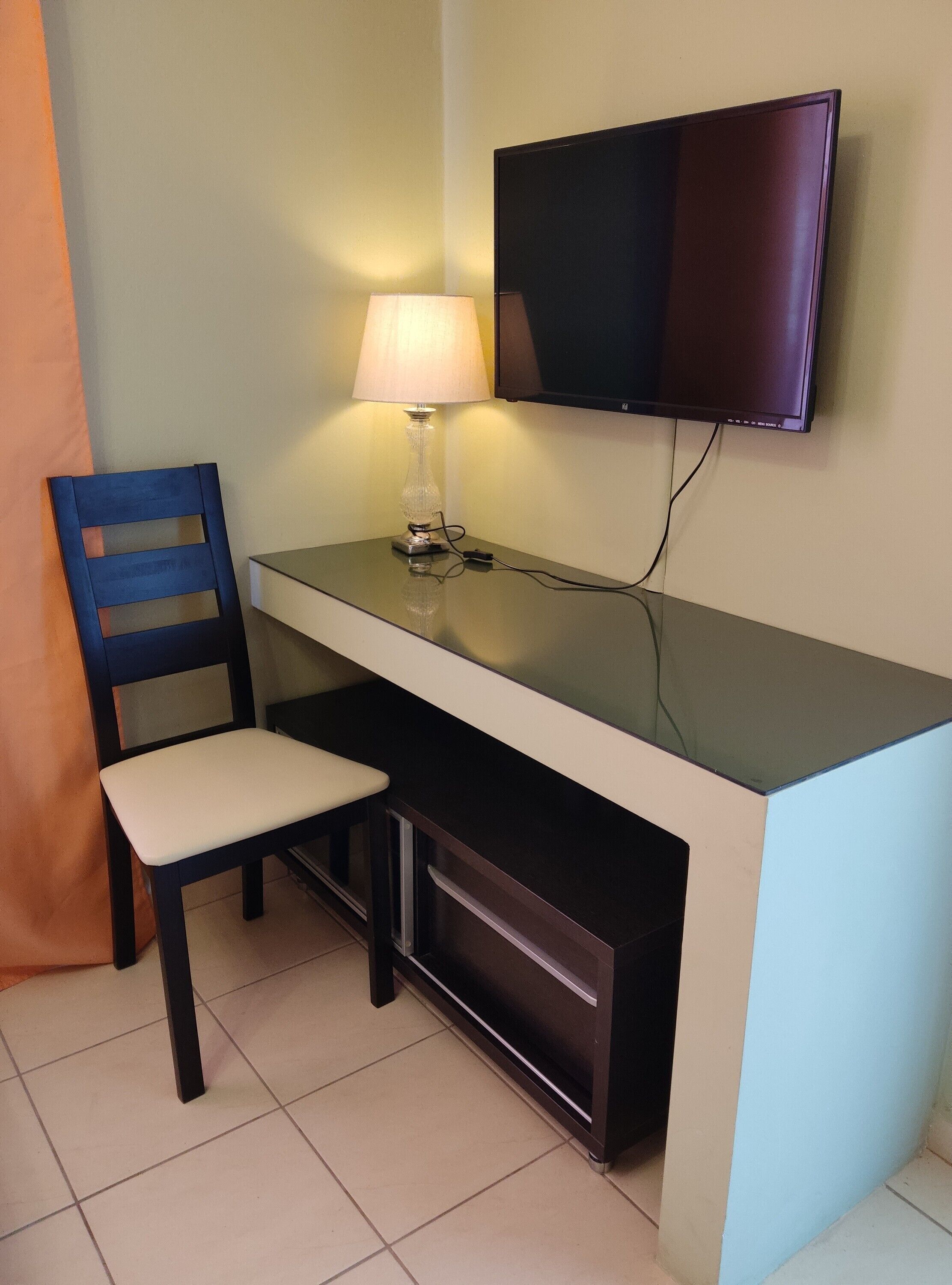 A small desk with a chair, a lamp, and a television mounted on the wall.