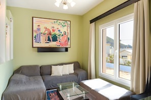 Una habitación con sofá, una mesa de centro de vidrio, un cuadro en la pared y una ventana con cortinas.