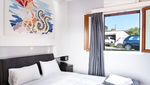 Habitación de hotel con cama, mesita de noche, teléfono, ventana con cortinas y vista a coches estacionados afuera.