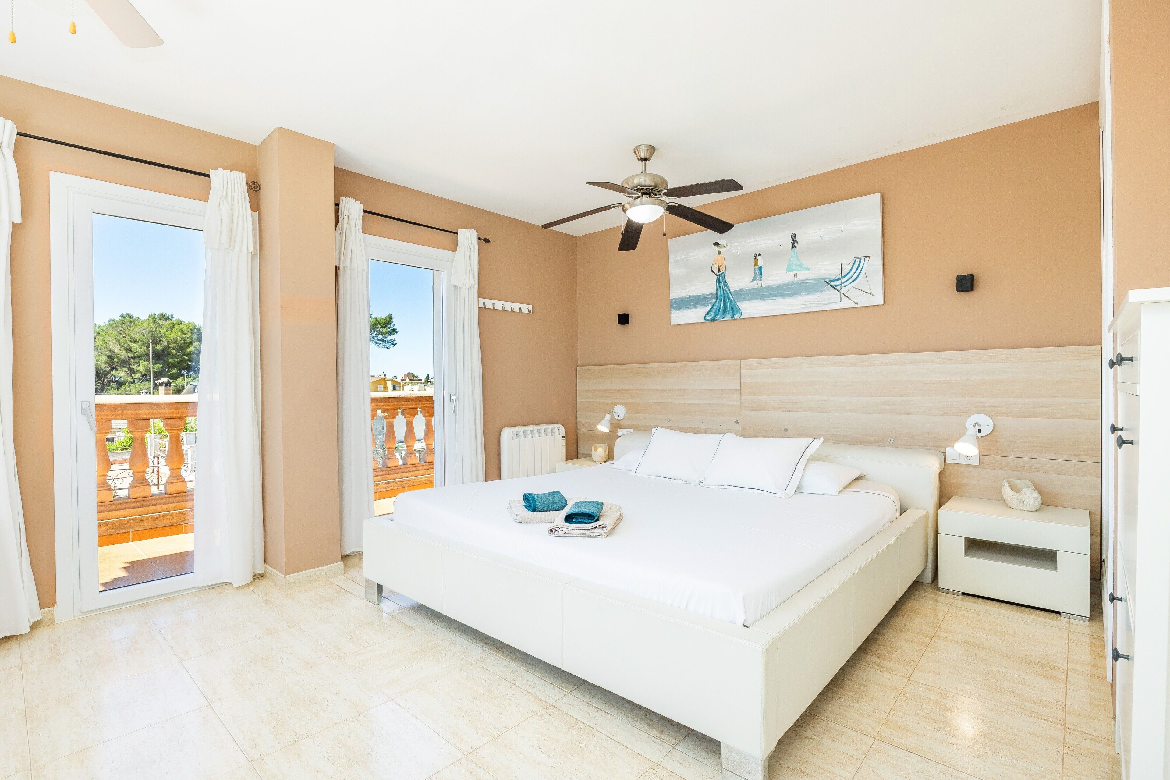 A bedroom with a large bed, a ceiling fan, a nightstand, and a painting on the wall.