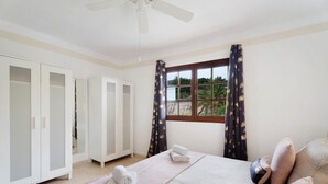 A bedroom with a bed, a wardrobe, a window with curtains, and a view of greenery outside.