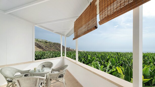 A balcony with wicker furniture, a view of green fields, and a coastal landscape.