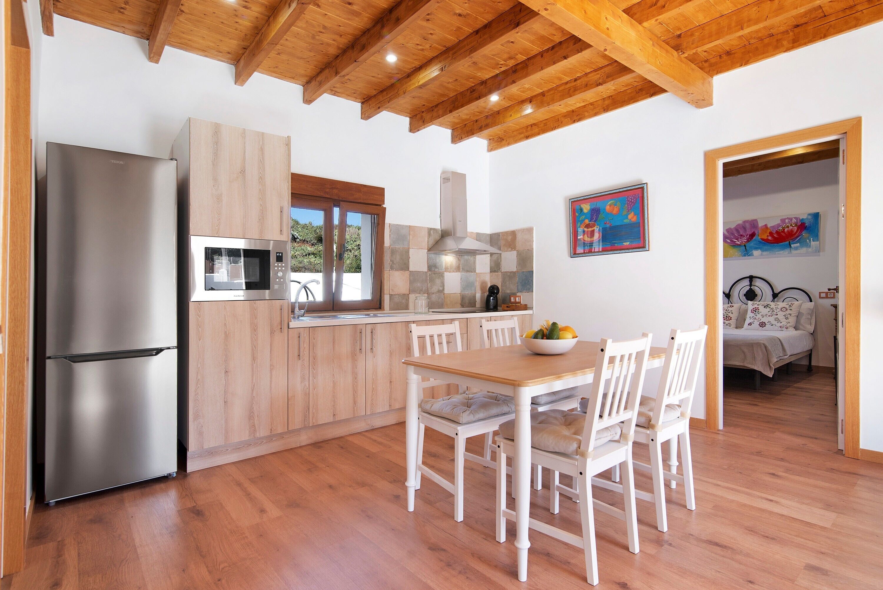 Una cocina moderna con refrigerador de acero inoxidable, armarios de madera y un comedor con sillas blancas y una mesa de madera.