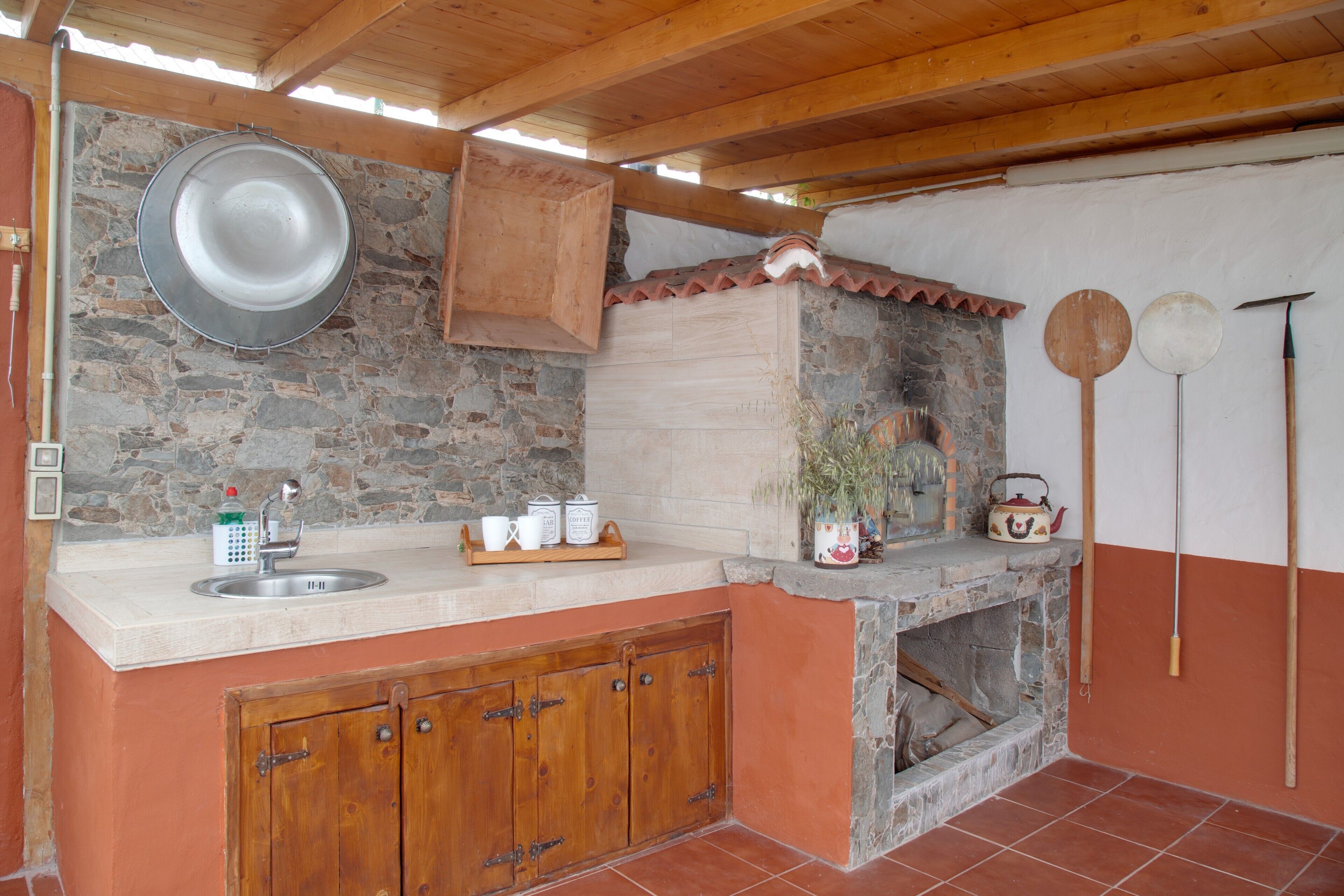 A rustic kitchen with a stone wall, wooden cabinets, and a tiled floor.