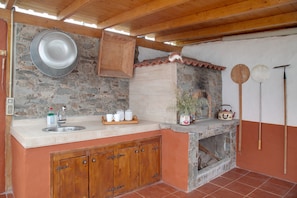 A rustic kitchen with a stone wall, wooden cabinets, and a tiled floor.