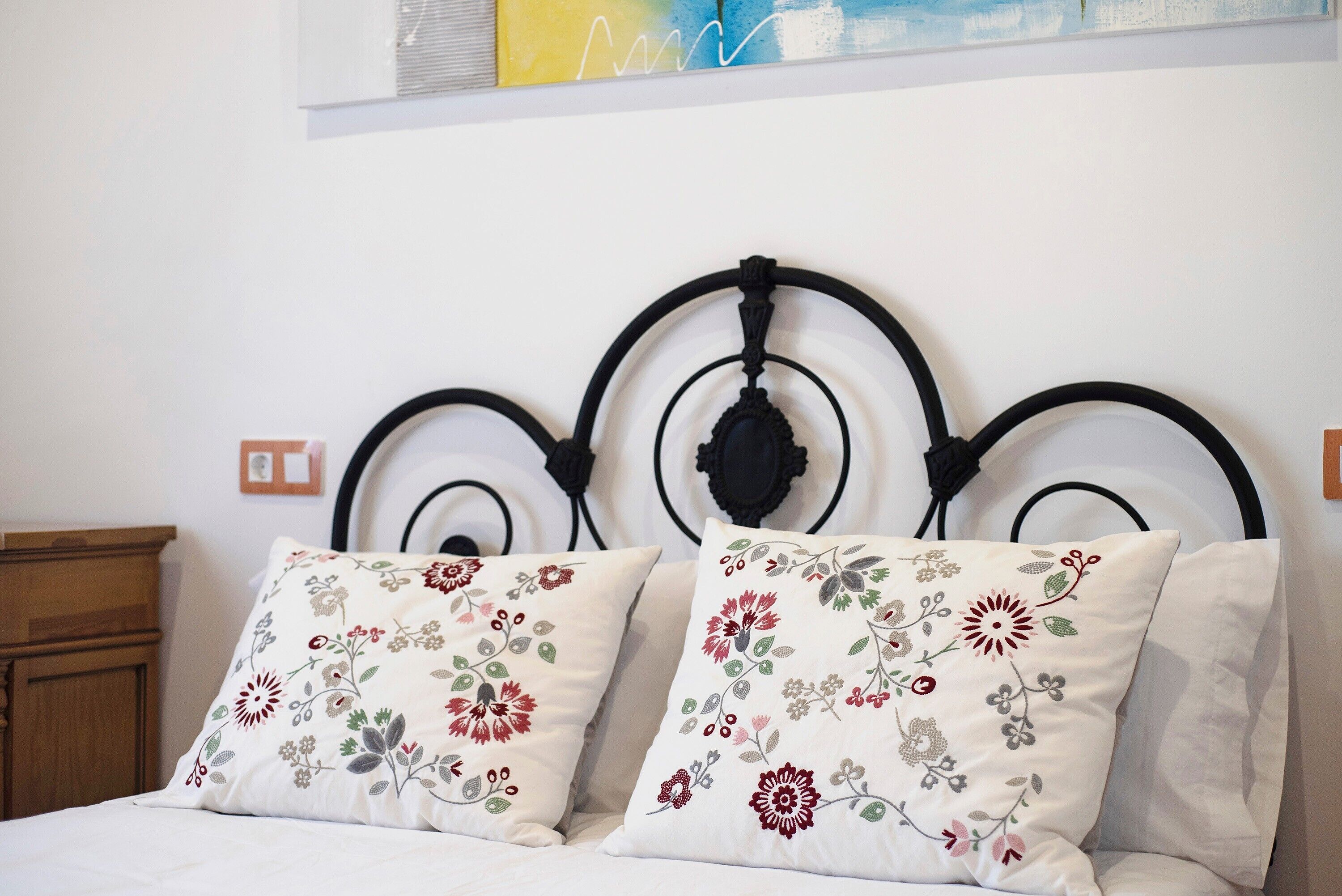 A bed with a metal headboard and two pillows with floral embroidery.