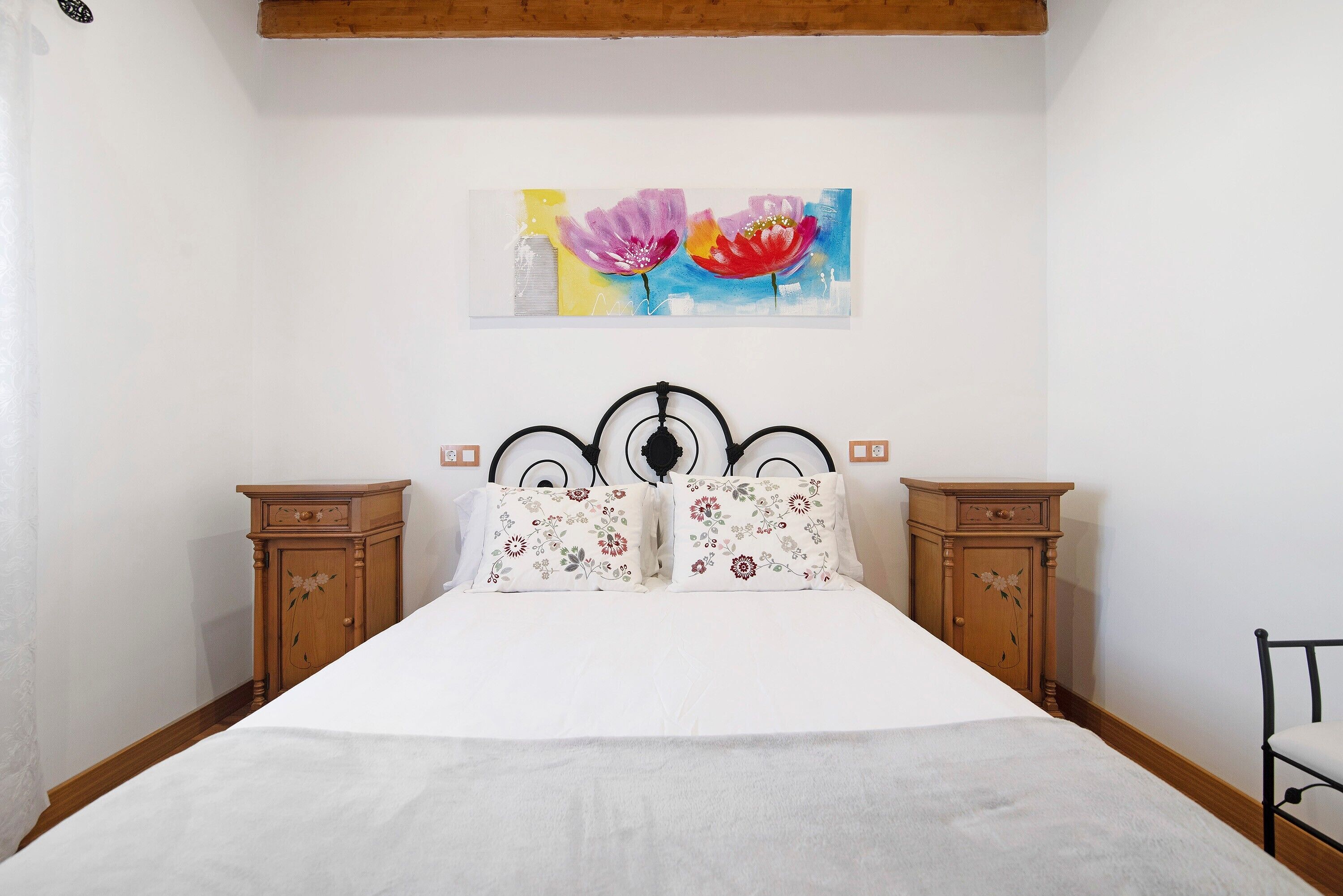 Een slaapkamer met een bed, twee nachtkastjes, een houten hoofdeinde en een schilderij aan de muur.