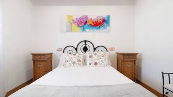 Een slaapkamer met een bed, twee nachtkastjes, een houten hoofdeinde en een schilderij aan de muur.