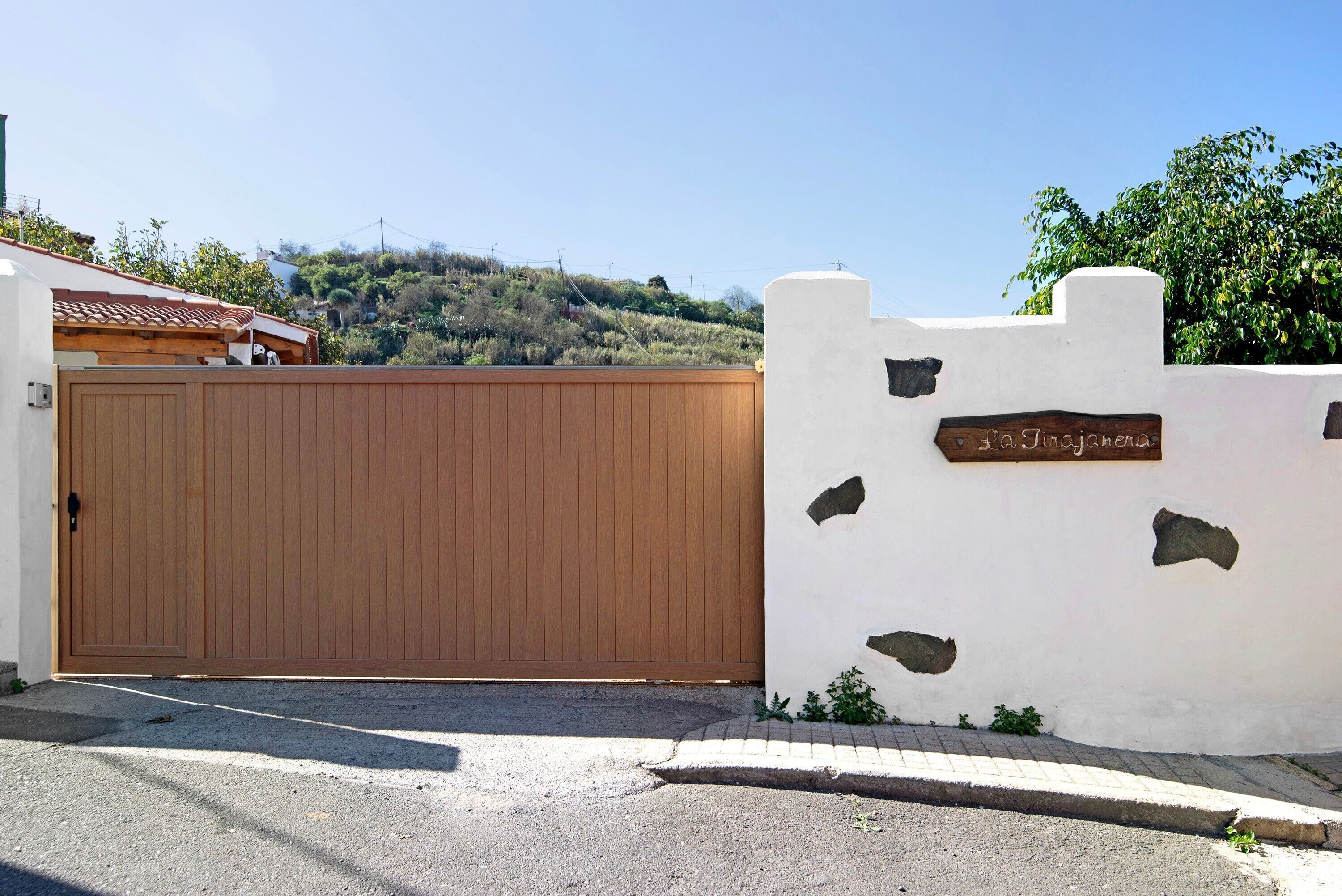 Una entrada protegida por un portón con una puerta de madera, un muro blanco con parches de piedra, y un cartel que dice 'la Jaizneta'.