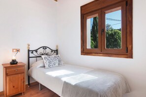 A single bed with a headboard, a bedside table with a lamp, and a window with a view of greenery.