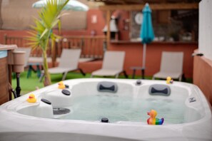 A hot tub with rubber ducks and a patio area with chairs and a palm tree.
