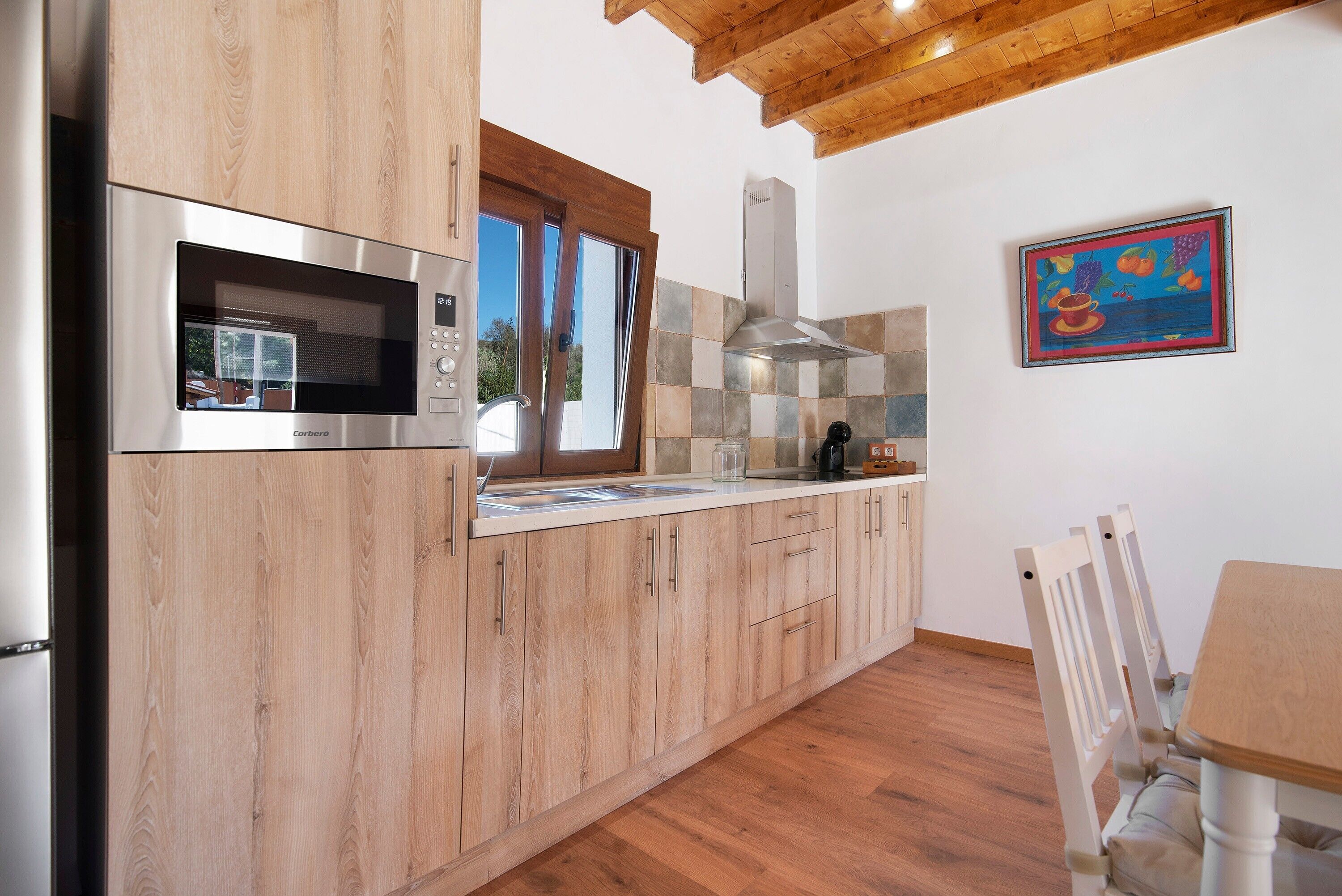 Una cocina moderna con muebles de madera, un microondas de acero inoxidable y un ventanal.