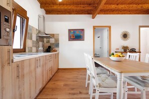 Una cocina con armarios de madera, encimera blanca y una zona de comedor con mesa de madera y sillas blancas.